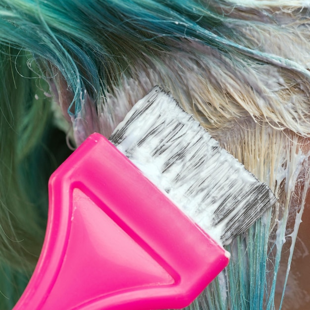 Parrucchiere che usa la spazzola rosa mentre applica la vernice alla cliente femminile con il colore dei capelli color smeraldo durante