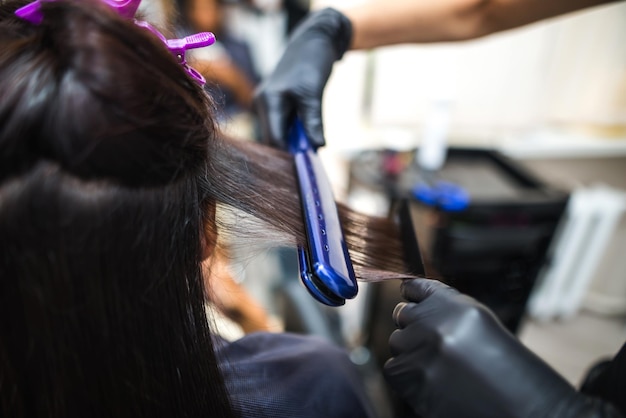 Parrucchiere che utilizza un capello stirato per raddrizzare i capelli Parrucchiere che lavora sull'acconciatura di una donna al saloneCura dei capelli Bella donna attraente in un salone di bellezza