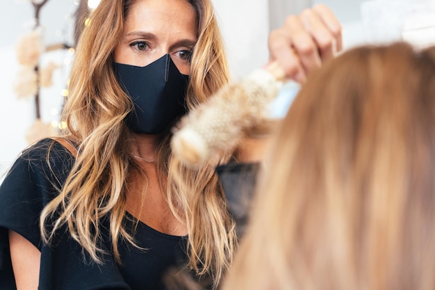 Parrucchiere con maschera facciale che asciuga i capelli di un cliente