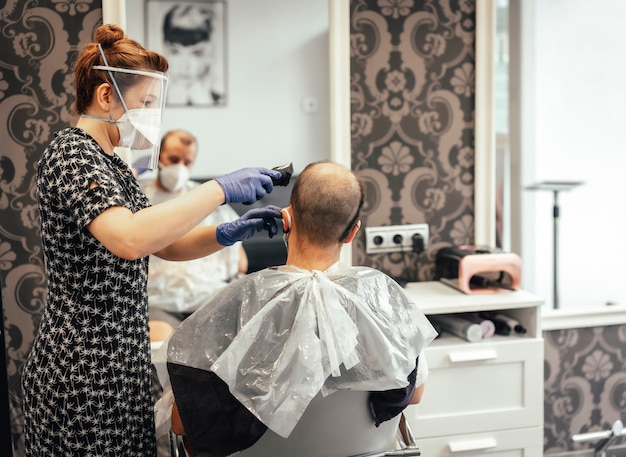 Parrucchiere con misure di sicurezza per il covid-19, nuova normalità, distanza sociale, taglio dei capelli con una maschera protettiva