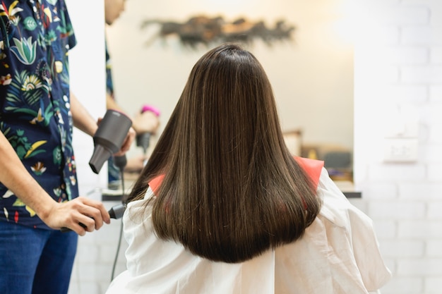 Parrucchiere dello stilista che fa acconciatura facendo uso dell&#39;asciugacapelli che soffia sui capelli del cliente