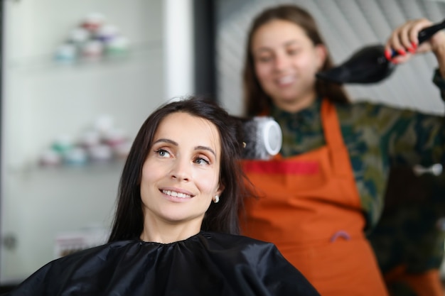 Parrucchiere donna che asciuga e raddrizza i capelli del cliente con spazzolatura e asciugacapelli. Concetto di cura dei capelli