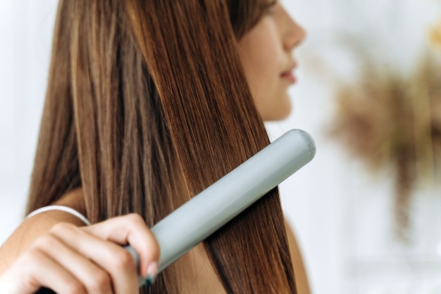 Parrucchiere. Donna con bei capelli lunghi e lisci con piastra per capelli. Ragazza splendida che raddrizza i capelli sani con il ferro da stiro. Concetto di stiratura e acconciatura dei capelli