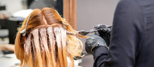 Parrucchiere femminile che tinge i capelli di giovane donna caucasica nel salone di capelli