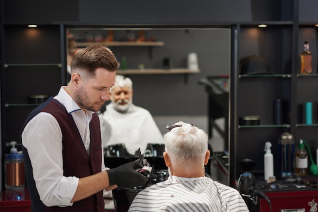 Parrucchiere in guanti neri che tagliano il taglio di capelli dell'uomo.