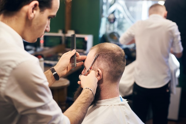 Parrucchiere maschio che fa un taglio di capelli corto per il cliente in un moderno barbiere Concetto di taglio di capelli tradizionale con le forbici