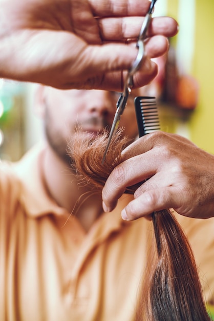 Parrucchiere maschio che lavora in un salone di bellezza e che taglia le punte dei capelli di una cliente femminile.