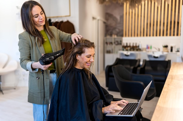 Parrucchiere professionista che asciuga i capelli del cliente che lavora in remoto sul laptop