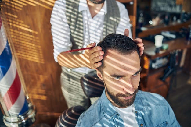 Parrucchiere professionista che fissa la posizione della testa del suo cliente in un barbiere