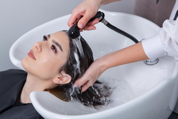parrucchiere professionista che lava i capelli della giovane donna nel salone di bellezza