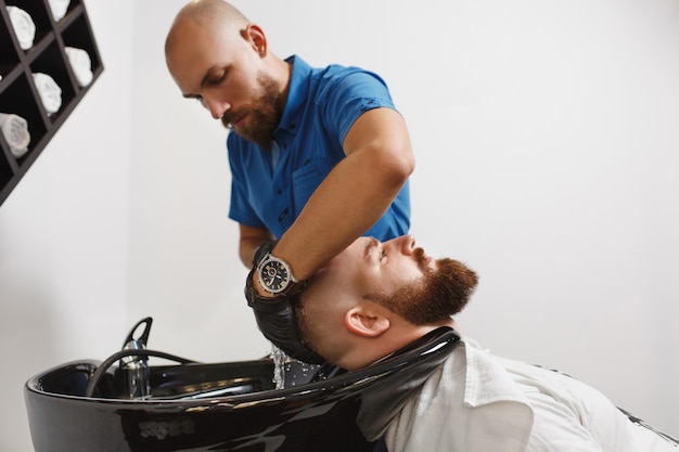 Parrucchiere professionista maschio che serve il cliente che lava la testa in un lavabo nero alla moda, asciugandosi con un asciugamano