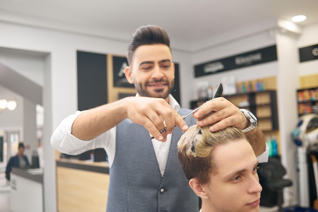 Parrucchiere sorridente che fa un hairdress per il giovane cliente nel salone beaty.