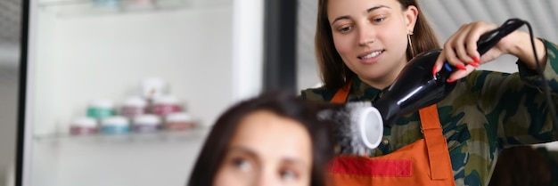 Parrucchiere sorridente che usa l'asciugacapelli per il trattamento dei capelli ed è creativo