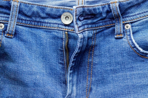 Parte anteriore dei jeans con bottone aperto e tasche della chiusura lampo Fondo blu brillante della struttura del tessuto del denim Vista del primo piano