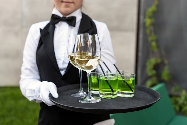 Parte centrale del cameriere professionista in uniforme che serve vino durante la festa di catering a buffet, eventi festivi o matrimoni. Bicchieri pieni di champagne sul vassoio. Servizio di catering per feste all'aperto, cameriere di turno.