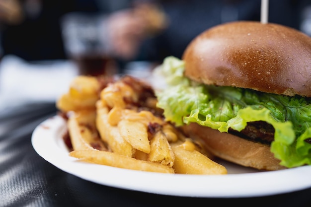 Parte del primo piano dell'hamburger gourmet con patatine fritte in tavola con persone irriconoscibili sullo sfondo