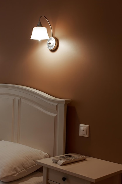 Parte dell'interno della camera da letto? mostrando la parte del letto e la lampada da parete sul muro beige