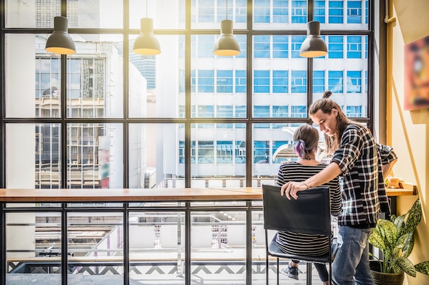 Parte delle giovani free lance delle coppie dei pantaloni a vita bassa che lavorano nel posto di lavoro del caffè del sottotetto