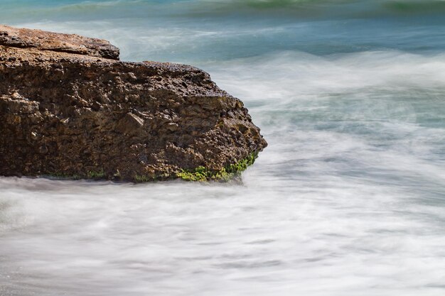 Parte di roccia di pietra in mare sul litorale movimento dell'acqua sfocato