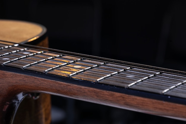 Parte di una chitarra acustica, tastiera per chitarra con corde su sfondo nero con riflessi.