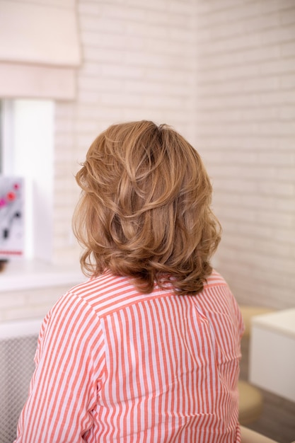 Parte posteriore della femmina con capelli biondi ricci nel salone di parrucchiere