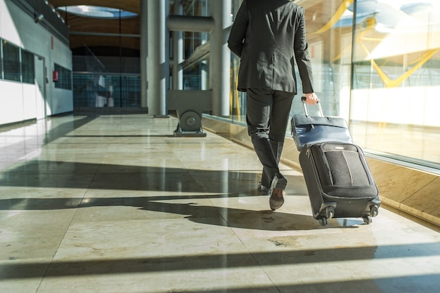 Parte posteriore e gambe dell'uomo d'affari che camminano con i bagagli all'aeroporto