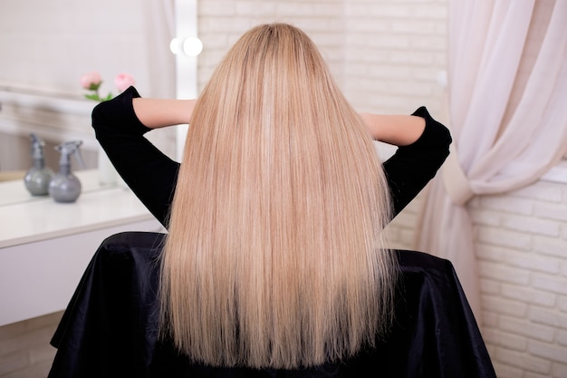 Parte posteriore femminile con capelli biondi lunghi dritti nel salone di parrucchiere