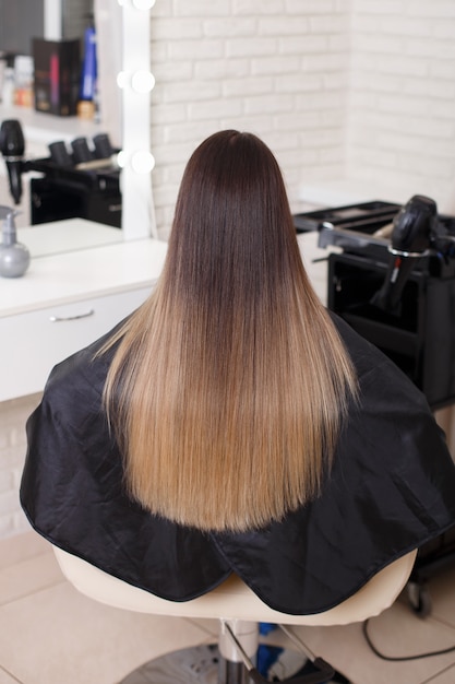 Parte posteriore femminile con capelli castani ombre lunghi dritti nel salone di parrucchiere