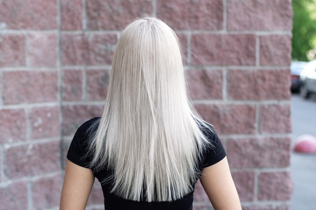 Parte posteriore femminile con capelli lunghi, lisci, sani, biondi, su sfondo stradale