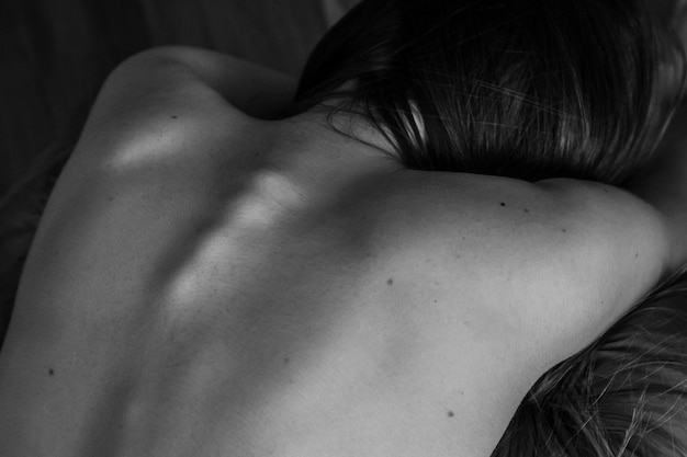 Parte posteriore nuda di giovane femmina sensuale depressa che si siede sul pavimento con la schiena nuda