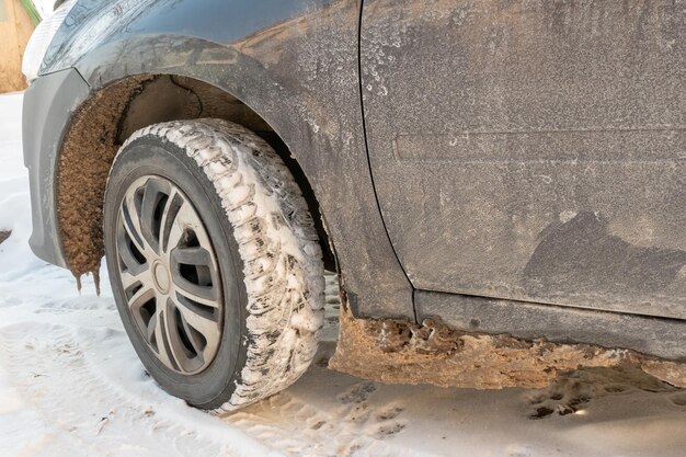 Parti dell'auto sono ricoperte di neve e ghiaccio dopo una nevicata Primo piano della ruota in sporcizia e reagenti antighiaccio Grandi gelate e molta neve in città Problemi sulle strade scivolose invernali