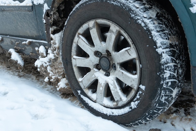 Parti dell'auto sono ricoperte di neve e ghiaccio dopo una nevicata Primo piano della ruota in sporcizia e reagenti antighiaccio Grandi gelate e molta neve in città Problemi sulle strade scivolose invernali