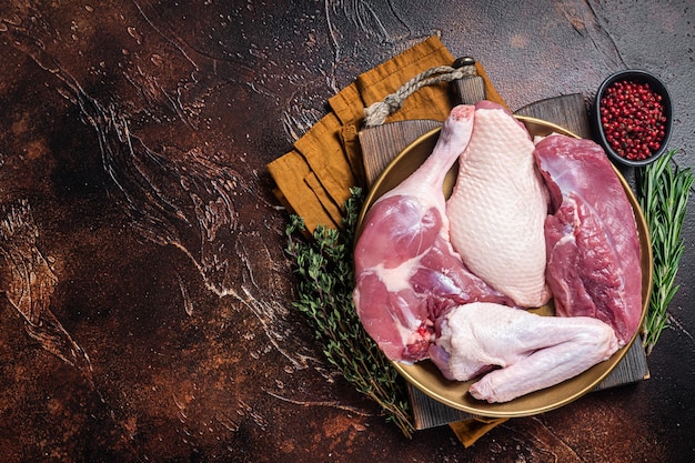 Parti di carne fresca di anatra gambe di bistecca di petto crudo ali in un piatto con erbe Sfondo scuro Vista dall'alto Spazio di copia