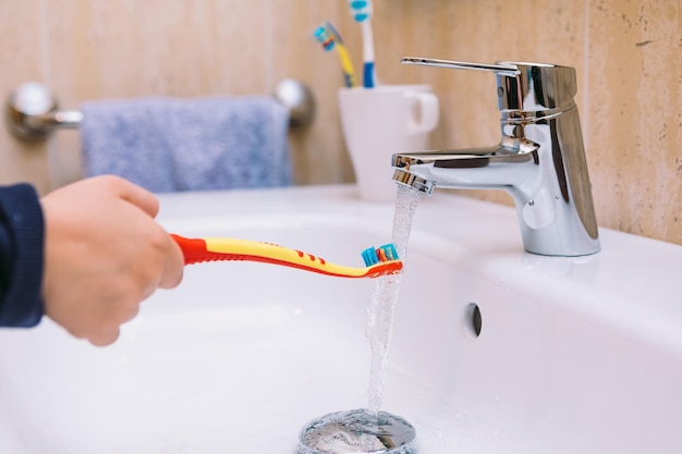 Particolare del braccio di una bambina in bagno, che versa acqua sullo spazzolino nel lavandino. Spazzolatura dei denti, igiene e concetto di infanzia.