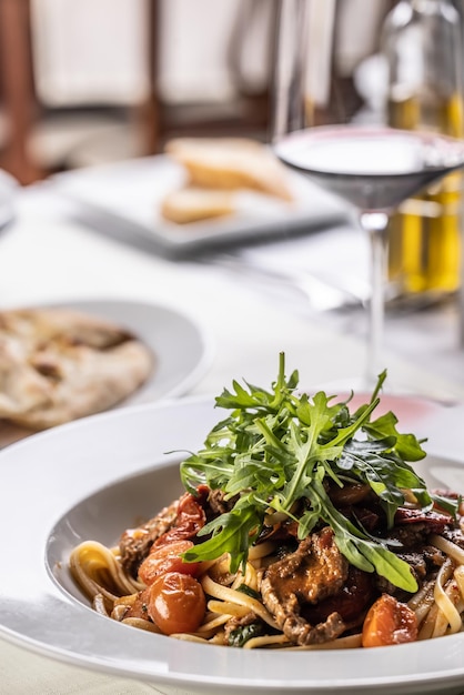 Particolare delle linguine di carne con pomodori e rucola servite con vino su un tavolo della caffetteria