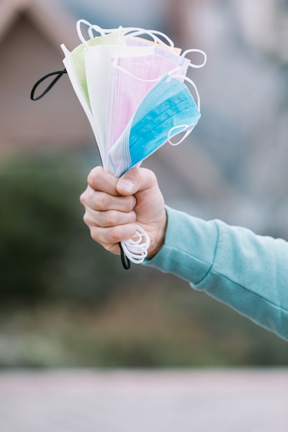 Particolare di un braccio che regge una manciata di mascherine chirurgiche colorate. Concetto Covid-19