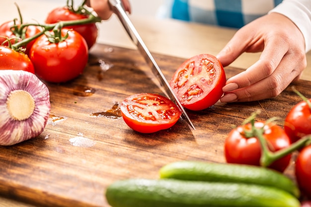 Particolare di un pomodoro appena tagliato a metà su un tagliere con a parte cetriolo, aglio e altri pomodori.