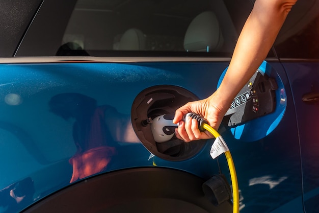 Particolare di una mano che tiene un'auto elettrica che carica le batterie nel garage di casa