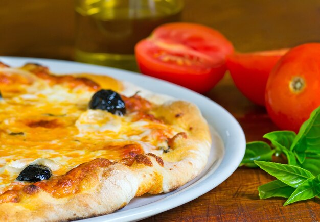 Particolare di una pizza su un tavolo di legno con ingredienti tutt'intorno