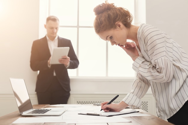 Partner commerciali che lavorano in ufficio. Manager seri e stanchi che sviluppano strategie di marketing sul posto di lavoro moderno con laptop e documenti, spazio copia, messa a fuoco selettiva