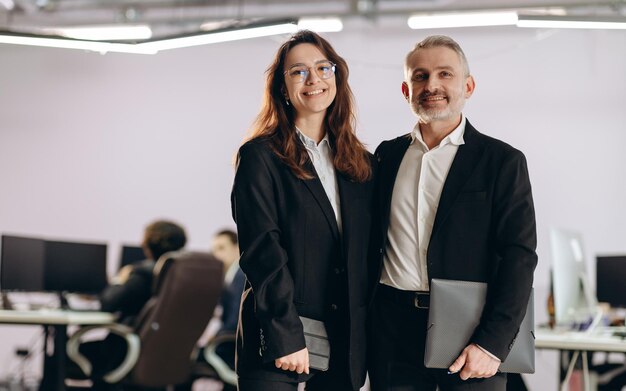 Partner commerciali felici con la cartella che presentano insieme Sorridente imprenditrice e uomo d'affari in piedi nello spazio ufficio