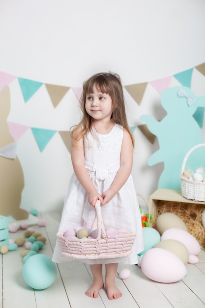 Pasqua! Bella bambina in abito bianco con un cesto con uova di Pasqua colorate e coniglietti pasquali. Decorazioni pasquali, decorazioni primaverili. Vacanze in famiglia, tradizioni. Piccolo contadino. Raccolta