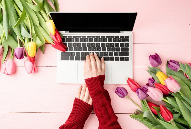 Pasqua e concetto di primavera. Mani della donna che digitano sulla tastiera del computer portatile. Spazio di lavoro femminile decorato con tulipani