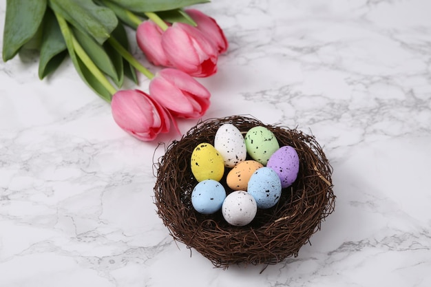 Pasqua primavera ancora vita Nido con uova colorate e tulipani rosa su una superficie di marmo