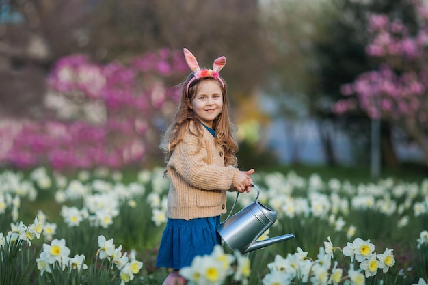 Pasqua Una bambina carina di 5 anni con orecchie di coniglio innaffia i narcisi sul prato Bambino felice Vacanze primaverili