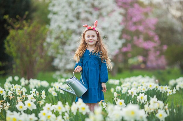 Pasqua Una bambina carina di 5 anni con orecchie di coniglio innaffia i narcisi sul prato Bambino felice Vacanze primaverili