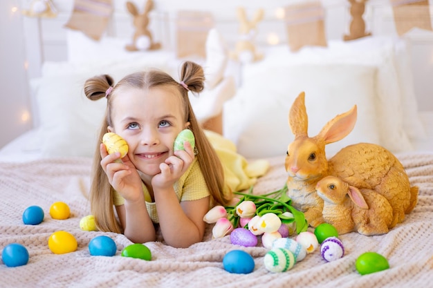 Pasqua una bambina con le uova colorate dipinte tulipani e un coniglio a casa in una stanza luminosa si sta preparando per la vacanza sorridendo divertendosi e giocando con le uova chiudendo gli occhi