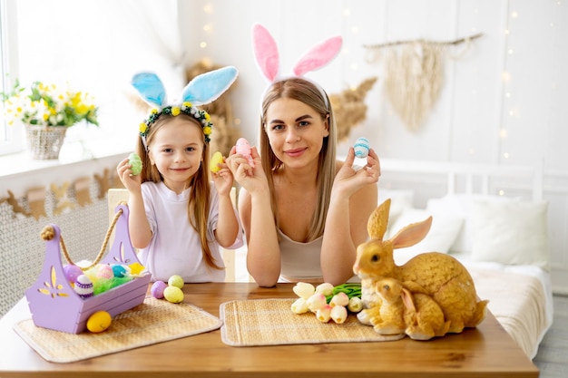 Pasqua una madre con una bambina con le orecchie di lepre sulla testa si stanno preparando per la festa colorando le uova e giocando con loro stile di vita preparando una famiglia felice con un bambino per Pasqua