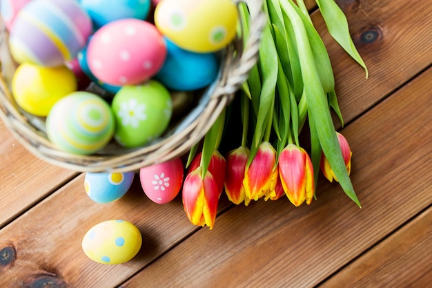 pasqua, vacanze, tradizione e concetto di oggetto - primo piano di uova di pasqua colorate nel cesto e fiori di tulipano su tavolo di legno con spazio per la copia