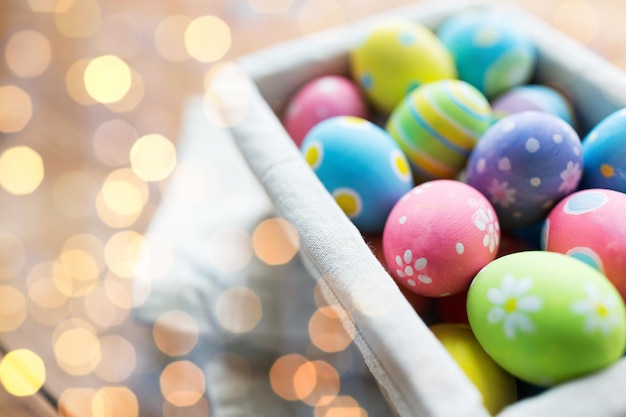 pasqua, vacanze, tradizione e concetto di oggetto - primo piano di uova di pasqua colorate nel cesto sopra le luci delle vacanze